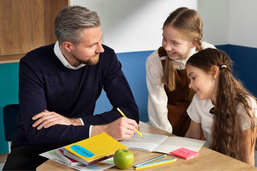 Teacher and Students: Teacher tutoring two girls at a table.